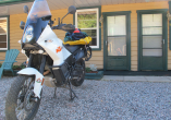 white motorcycle in front of motel with brown siding and green doors
